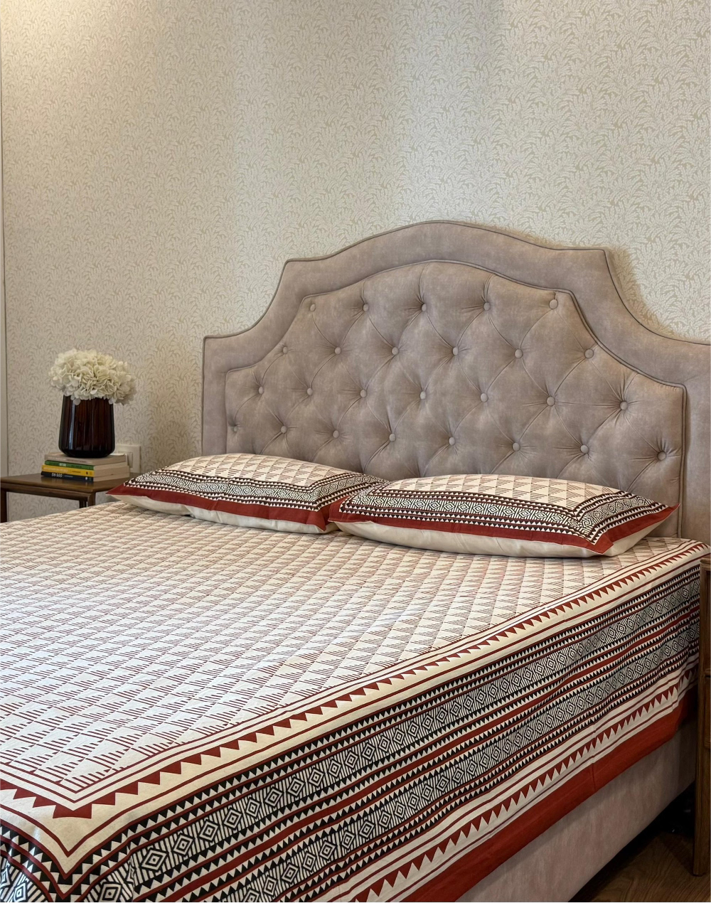 Bed with patterned bedding and tufted headboard in a room.